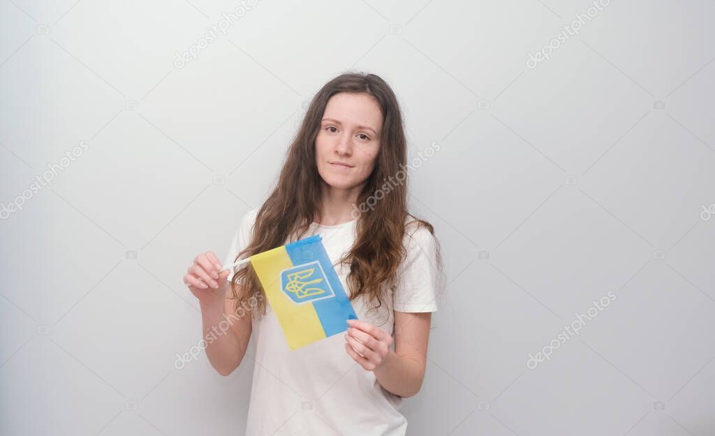 Young beautiful girl in embroidered shirt with Ukrainian flag. Attractive Ukrainian woman wearing traditional Ukrainian embroidery on the grey background.