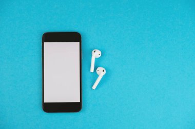 Mavi arka planda kablosuz kulaklıklı cep telefonu..