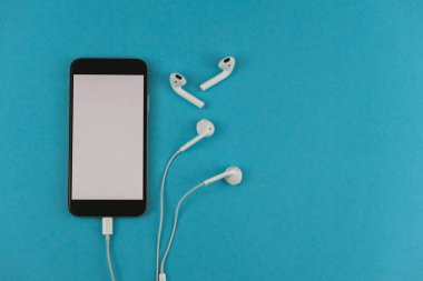Kulaklıklı cep telefonu ve mavi arka planda kablosuz kulaklık..