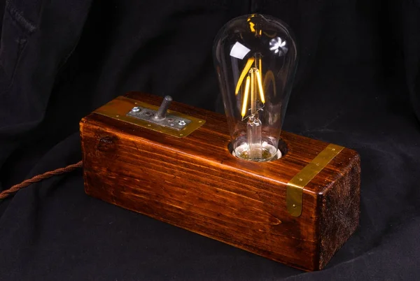 Light fixture handmade in vintage style, wooden case, copper finish, led lamp on a black background.