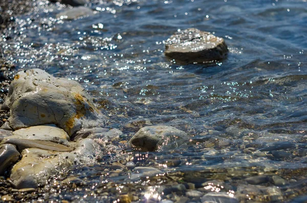 pebble stones on the sea beach on a warm summer day, the rolling waves of the blue sea with white foam