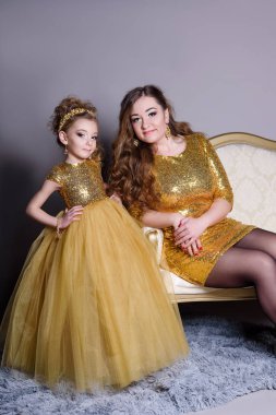 küçük güzel gülümseyen bebek annesiyle bir akıllı elbise Haritayı kostüm takı kendiniz için bir büyük altın kanepe ve kabarık gri halı gri bir arka plan üzerinde