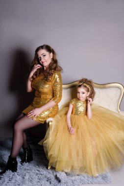 küçük güzel gülümseyen bebek annesiyle bir akıllı elbise Haritayı kostüm takı kendiniz için bir büyük altın kanepe ve kabarık gri halı gri bir arka plan üzerinde