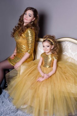 küçük güzel gülümseyen bebek annesiyle bir akıllı elbise Haritayı kostüm takı kendiniz için bir büyük altın kanepe ve kabarık gri halı gri bir arka plan üzerinde