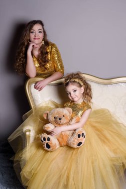 küçük güzel gülümseyen bebek annesiyle bir akıllı elbise Haritayı kostüm takı kendiniz için bir büyük altın kanepe ve kabarık gri halı gri bir arka plan üzerinde