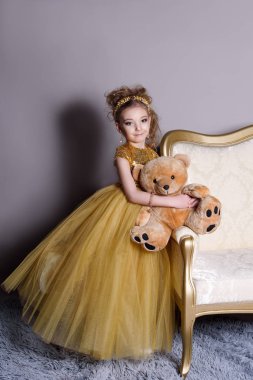 küçük güzel gülümseyen bebek akıllı elbise mücevher kendisi üzerinde büyük altın kanepe ve kabarık gri halı gri bir arka plan üzerinde gösterir