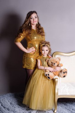 küçük güzel gülümseyen bebek annesiyle bir akıllı elbise Haritayı kostüm takı kendiniz için bir büyük altın kanepe ve kabarık gri halı gri bir arka plan üzerinde