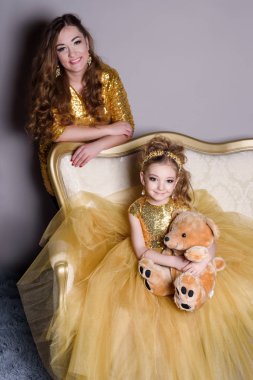 küçük güzel gülümseyen bebek annesiyle bir akıllı elbise Haritayı kostüm takı kendiniz için bir büyük altın kanepe ve kabarık gri halı gri bir arka plan üzerinde