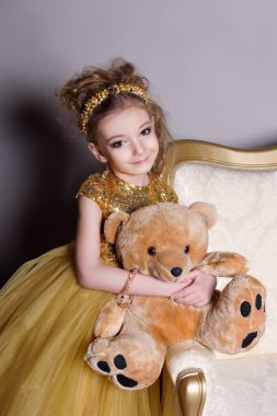 küçük güzel gülümseyen bebek akıllı elbise mücevher kendisi üzerinde büyük altın kanepe ve kabarık gri halı gri bir arka plan üzerinde gösterir