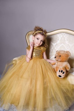 küçük güzel gülümseyen bebek akıllı elbise mücevher kendisi üzerinde büyük altın kanepe ve kabarık gri halı gri bir arka plan üzerinde gösterir