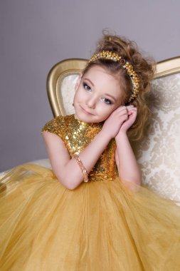 küçük güzel gülümseyen bebek akıllı elbise mücevher kendisi üzerinde büyük altın kanepe ve kabarık gri halı gri bir arka plan üzerinde gösterir