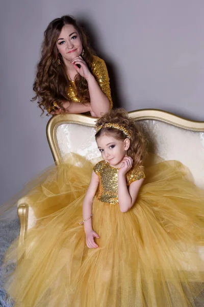 küçük güzel gülümseyen bebek annesiyle bir akıllı elbise Haritayı kostüm takı kendiniz için bir büyük altın kanepe ve kabarık gri halı gri bir arka plan üzerinde