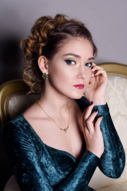 vasıl belgili tanımlık güzel altın koltuk takı göstermek gri bir arka plan üzerinde Yeşil kadife elbiseli güzel kız