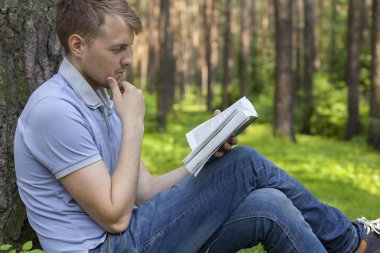 Genç bir adam bir yaz parkta bir kitap okuyor