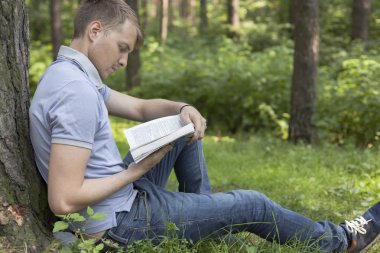 Genç bir adam bir yaz parkta bir kitap okuyor