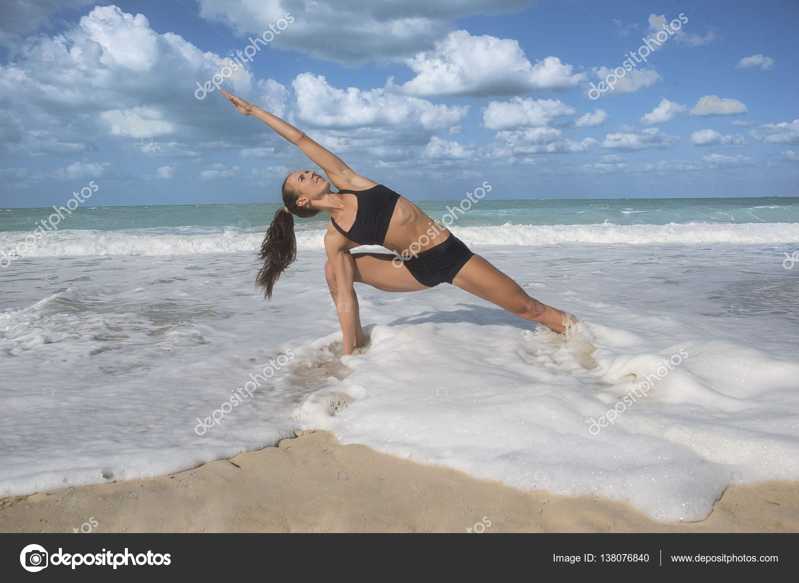 Girl in yoga pose with waves crashing over her legs on beach Stock