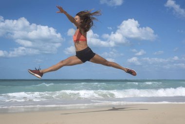 # Mavi gökyüzü ve beyaz bulutlar ile parlak güneşli bir günde beyaz kumlu bir plaj üzerinde sıçrayan dans kızı 