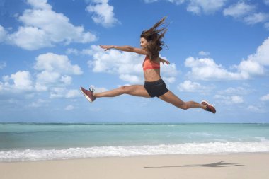 # Mavi gökyüzü ve beyaz bulutlar ile parlak güneşli bir günde beyaz kumlu bir plaj üzerinde sıçrayan dans kızı 