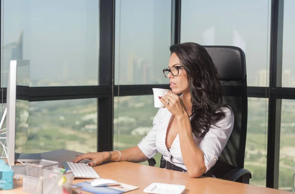 Beautiful Secretary or business woman in office with glasses sipping tea while at computer — Stock Photo, Image