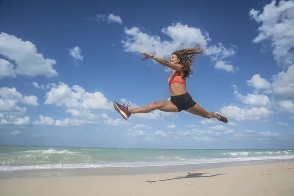 Menina dançando pulando em uma praia de areia branca em um dia ensolarado brilhante com céus azuis e nuvens brancas — Fotografia de Stock