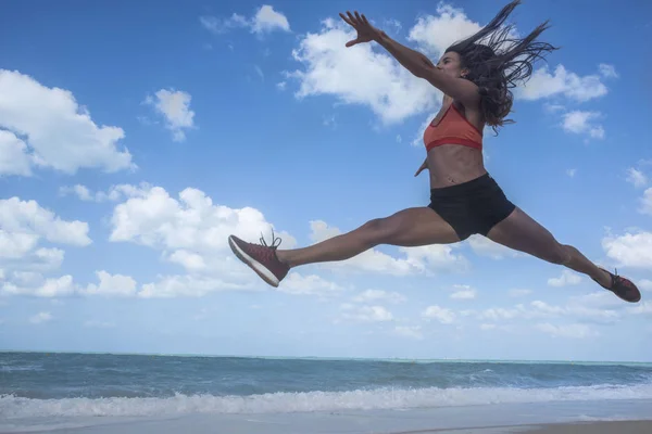 Ragazza che balla saltando su una spiaggia di sabbia bianca in una luminosa giornata di sole con cieli blu e nuvole bianche — Foto Stock