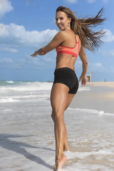 Vackra Europeiska tjej med långt hår, klädd i korta tights och topp kör bort på stranden — Stockfoto
