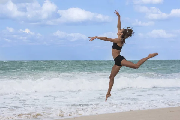 Bianca ragazza europea che balla saltando sulla spiaggia con pantaloncini neri stretti e top nero — Foto Stock