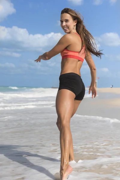 Hermosa chica corriendo por la playa riendo usando apretado negro pantalones cortos — Foto de Stock