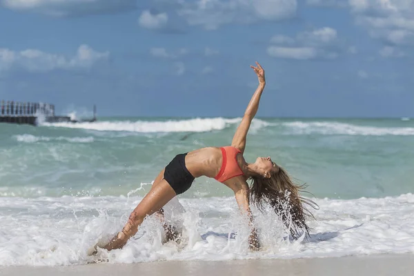 Ragazza in posa yoga con onde che si schiantano sulle gambe sulla spiaggia — Foto Stock