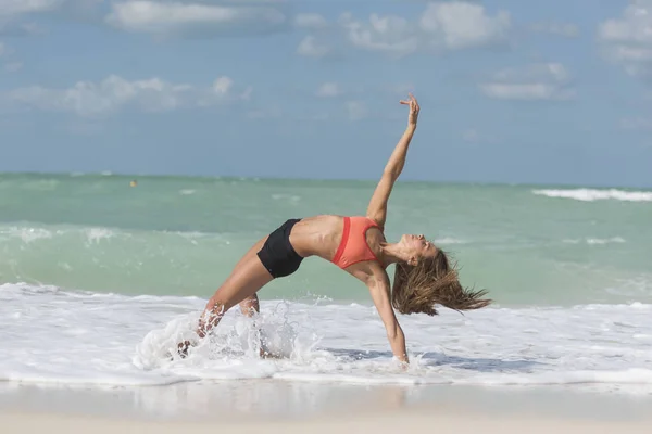 Ragazza in posa yoga con onde che si schiantano sulle gambe sulla spiaggia — Foto Stock
