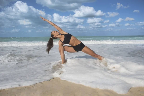 Girl in yoga pose with waves crashing over her legs on beach Stock