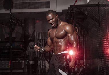 Kaslı, Afrikalı, üstsüz, terli erkek vücut geliştirme sporcusu. Kaslı, kirli bir spor salonunda halter kıvrımları yapıyor. 