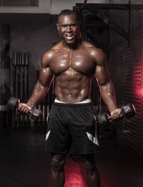 Kaslı, Afrikalı, üstsüz, terli erkek vücut geliştirme sporcusu. Kaslı, kirli bir spor salonunda halter kıvrımları yapıyor. 