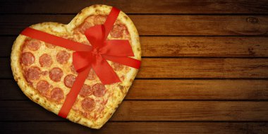 Siyah arka planda Sevgililer Günü için kırmızı kurdeleli pizza pepperoni şeklinde kalp. Üst Manzara. Tahta masada duran bayram yemeği kalbi.