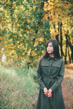 Dreamy beautiful girl with long natural black hair holding fallen leaves and walking in autumn forest