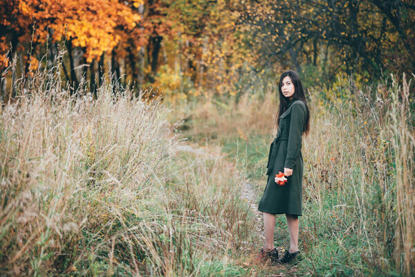 Dreamy beautiful girl with long natural black hair holding fallen leaves and walking in autumn forest