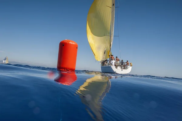 Sailing boat with yellow spinnaker and red buoy. Calm sea. — Stock Photo, Image