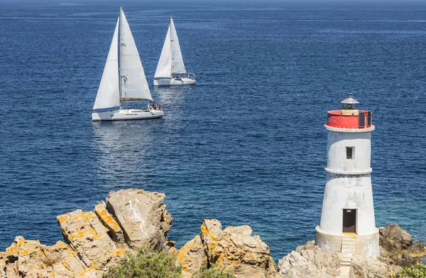 Two sailing boats with the rocks and white lighthouse — Stock Photo, Image