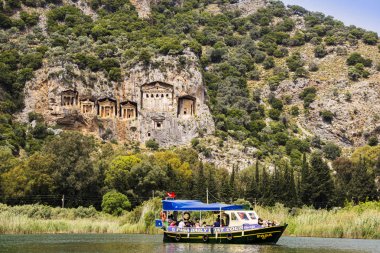 Dalyan, Türkiye - 16 Nisan 2018: nehir tekne turist Dalyan Likya mezar yıpranmış cephe ile dik kayalıklarla tarafından kesme Rock, yaklaşık M.ö. 400 Nehri üzerinde.