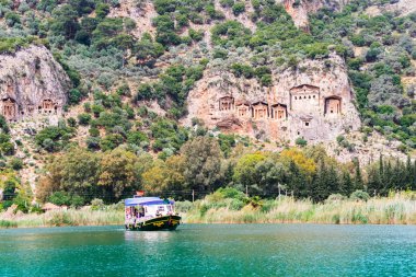 Dalyan, Türkiye - 16 Nisan 2018: nehir tekne turist Dalyan Likya mezar yıpranmış cephe ile dik kayalıklarla tarafından kesme Rock, yaklaşık M.ö. 400 Nehri üzerinde.
