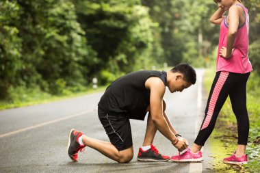 Koşan adam ayakkabılarını kız arkadaşına bağlıyor.