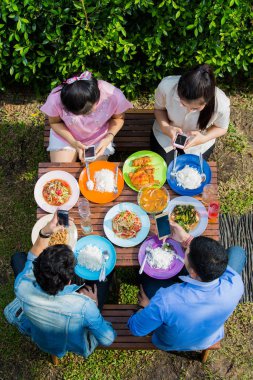 Asyalılar tatilde yemek yer, herkes telefonuna bakar. 