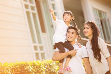 Asyalı bir aile. Mutlu bir kız. Ona bakmaları için ebeveynlerini işaret ediyor.