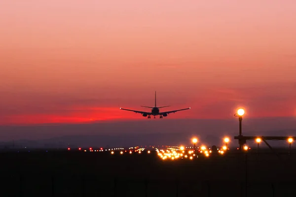 Plane lands at an airfield on the background of red clouds — Stock Photo, Image