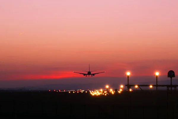 Avião pousando em um aeródromo no fundo de nuvens vermelhas — Fotografia de Stock