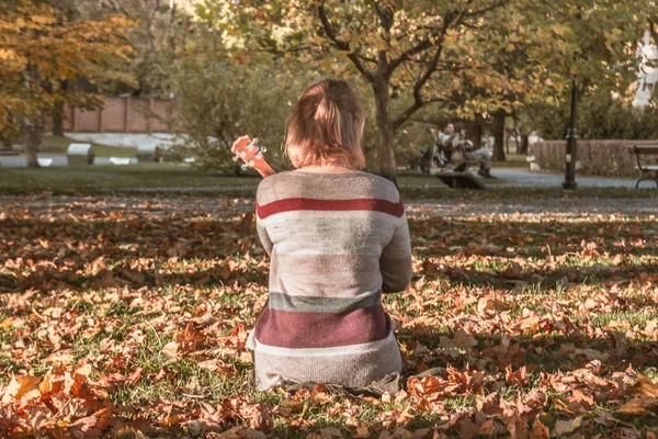 Chica con un ukelele sentado en otoño Parque — Foto de Stock