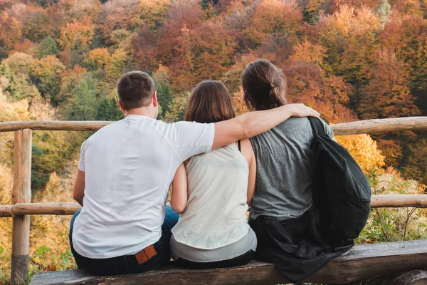 Ein Kerl umarmt zwei Mädchen, die auf die herbstliche Landschaft schauen — Stockfoto