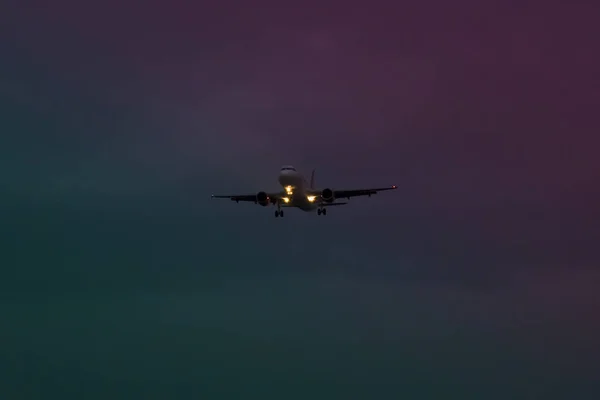 Bir uçak, gerçek dışı bir mor mavi ve yeşil ortasında akşam geceleri kapalı alıyor — Stok fotoğraf