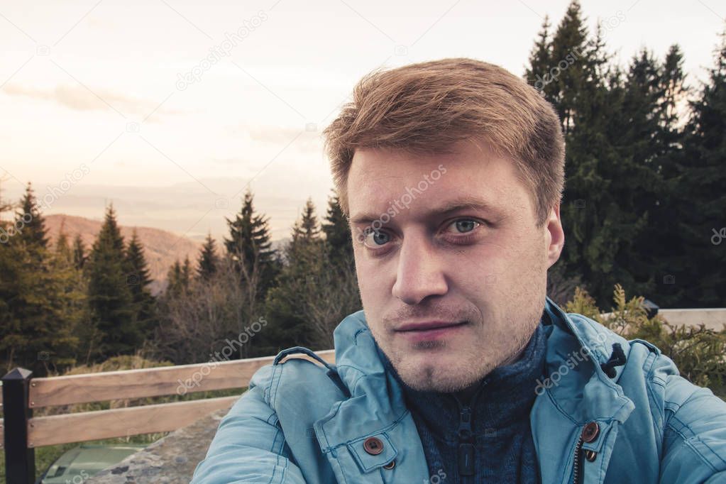 Portrait of a young handsome smiling guy who takes a selfie against a mountain landscape