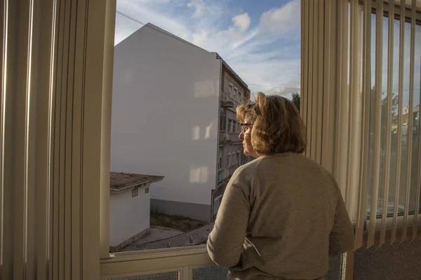 Mulher de meia-idade na janela com bela luz do pôr do sol — Fotografia de Stock